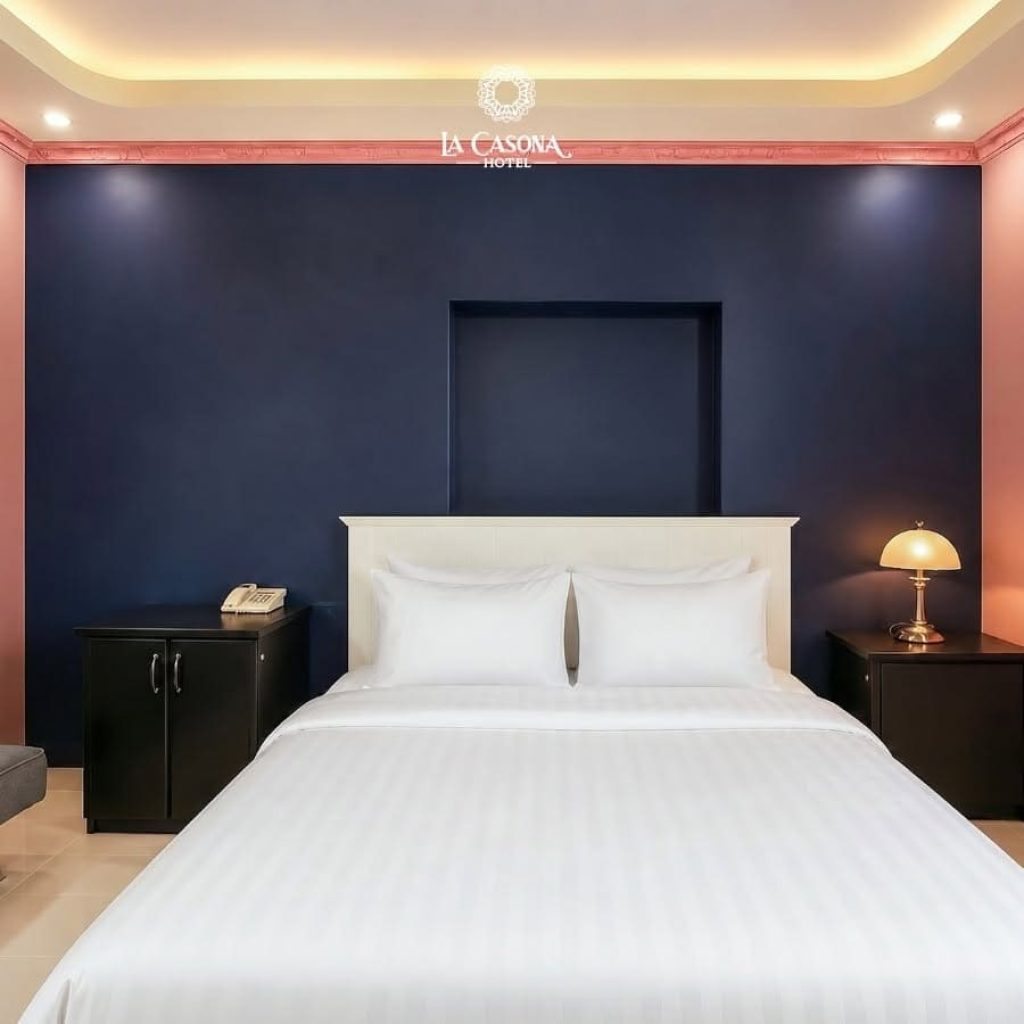 Cozy double bedroom with navy accent wall and ambient lighting at La Casona Hotel District 7